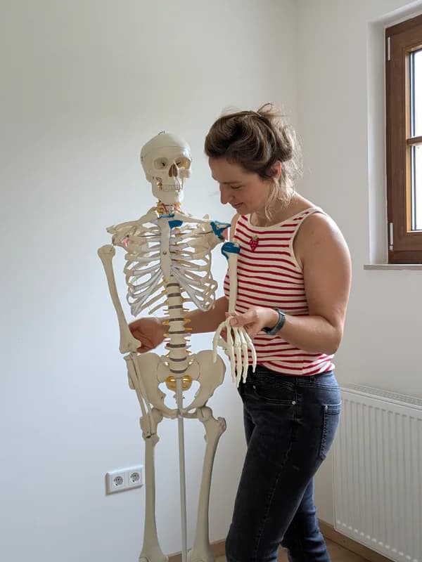 Zoé Goula-Kraus in der Praxis, die Hand eines anatomischen Skelettmodells haltend